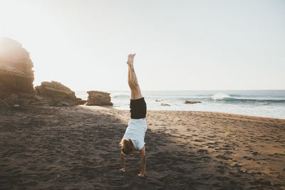 Man doing handstand on beach against clear sky