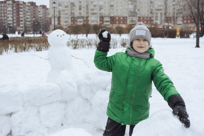 Happy boy standing inside snowcastle and play snowball game in winter park. winter fun in the snow