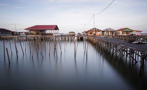 Stilt houses by river against sky