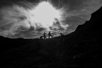 Hikers standing on mountain against cloudy sky
