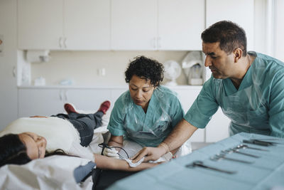 Male and female surgeons operating young woman lying on examination table in hospital