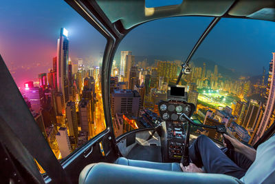 Midsection of pilot flying helicopter over illuminated city at night