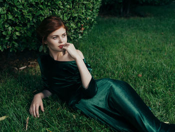 Young woman looking away while sitting on land