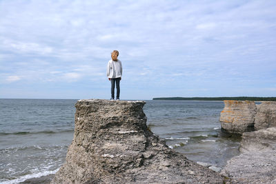 Rear view of woman standing on rock by sea against sky