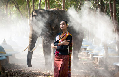 Smiling woman standing with elephant in forest