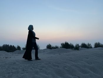 Full length of woman walking on sand against sky during sunset