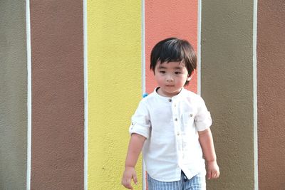 Cute baby boy standing against multi colored wall