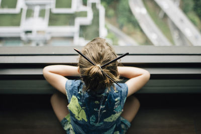 High angle view of girl with japanese hairpins looking through window while sitting at home