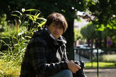 Man with dslr camera sitting by plant at park