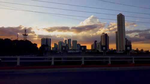 Bridge by buildings against sky during sunset