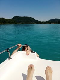 Low section of person relaxing on sea against clear sky