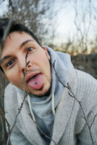 Close-up portrait of man sticking out tongue by bare tree