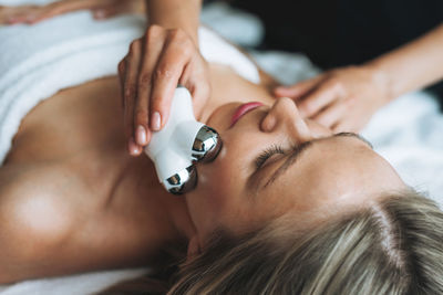 Young blonde woman enjoys facial massage with microcurrent facial massager in spa salon