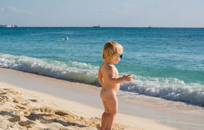 Full length side view of naked toddler standing on beach