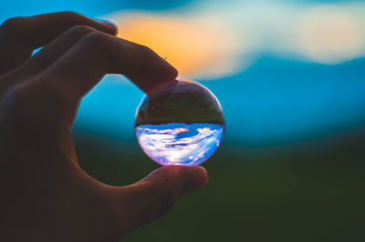 Close-up of hand holding crystal ball against sky