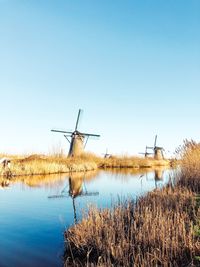 Traditional windmill by lake against clear sky