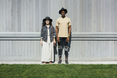 Man and woman wearing hat standing against wall