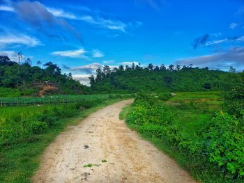 Dirt road amidst field against sky