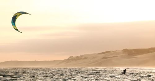 Man kiteboarding at sea against sky during sunset