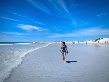 Full length of woman walking on shore at beach against blue sky
