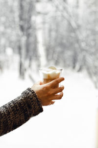 Woman holds glass glass with a cappuccino against the background of the winter forest.