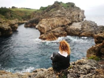 Rear view of woman sitting on cliff against sea