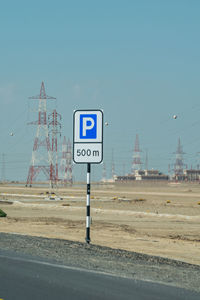 Road sign by street against clear blue sky