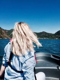 Woman in boat against sea and mountains against clear blue sky