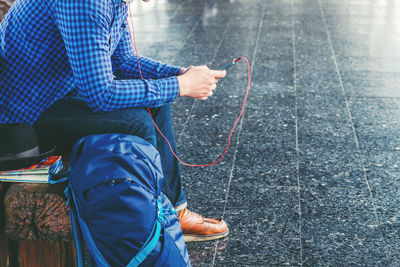 Low section of man with luggage listening music while sitting at railroad station platform