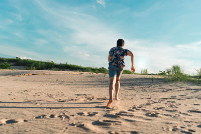 Rear view of man running on sand at beach