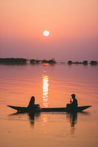 Silhouette people in lake against clear sky during sunset