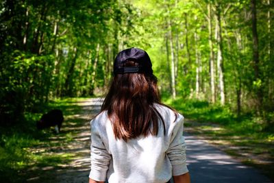 Rear view of young woman wearing cap walking on road in forest