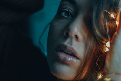 Close-up portrait of young woman with illuminated string lights