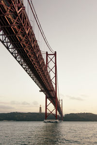 From below of red suspension bridge and river in lisbon in portugal against sky