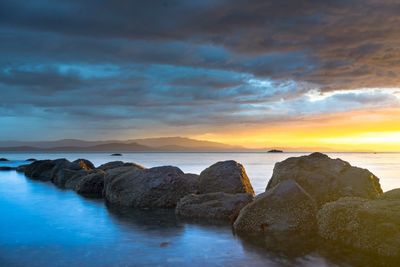 Rocks in sea against sky during sunset