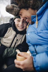 Happy father holding cup of tea embracing son in warm clothing