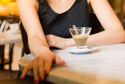 Midsection of woman holding drink sitting on table