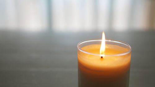 Close-up of lit candle on glass table