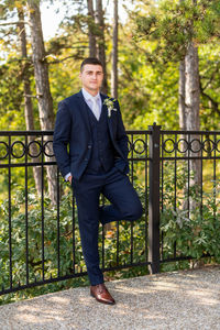 Handsome young groom wearing elegant dark blue suit looking at camera outdoors portrait. 