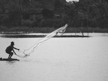 Man fishing in sea against trees