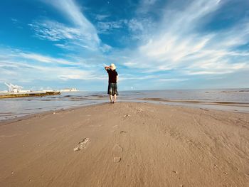 Rear view of man standing on beach against sky