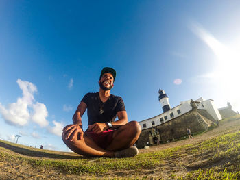 Low angle view of young man sitting on grass against sky