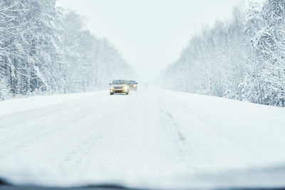 Snowy road in winter forest with moving car