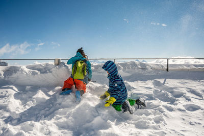 Kids playing in snow covered land during winter against sky