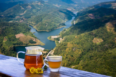 Jug glass of chrysanthemum juice on wooden terrace and natural landscapes background