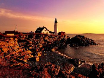 Lighthouse by sea against sky during sunset