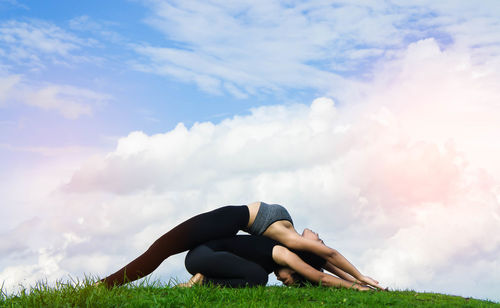 Friends exercising on grassy field against cloudy sky