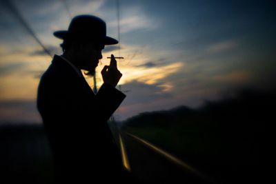 Side view of man holding cigarette while standing by railroad track on field