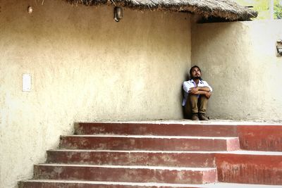 Young man looking up while sitting by house in village