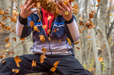 Midsection of man throwing dry leaves in forest